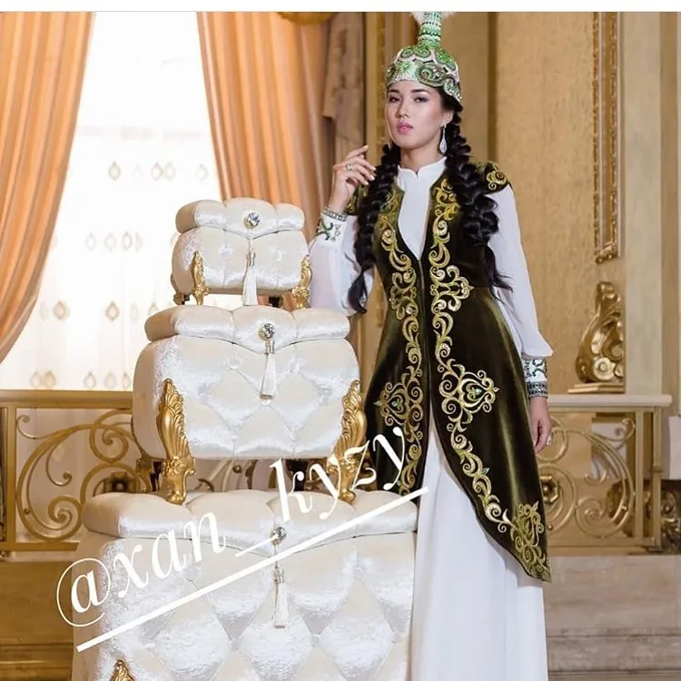 Woman in traditional dress beside a white and gold tiered dowry display