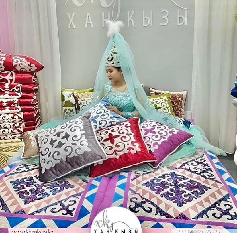 Model in a traditional Kazakh headdress reclining on colorful ornamental bedding